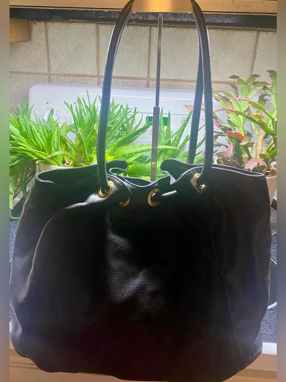 Michael Kors black leather handbag features a prominent gold circular logo charm